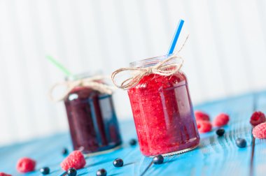 Glass mason jar with raspberry and blueberry jam. Fresh raspberries, blueberries on the blue wooden background.  Unique perspective, selective focus.