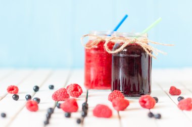 Rustic Mason Jars with raspberry jam and bog bilberry marmalade, fresh berries on white wooden background.  Selective focus
