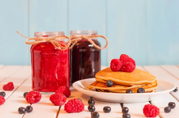 Stapel tarwe gouden pannenkoeken of pannenkoek taart met vers geplukt frambozen op een dessert bord, glazen Mason jar vol off Blueberry en framboos jam. — Stockfoto