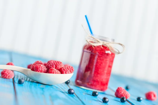 Raspberry smoothie in a glass mason jar and raspberries at wooden spon on light blue background. Light background, selective focus, Unique perspective — Stock Photo, Image
