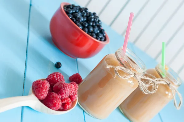 Homemade apricot smoothie in jam jar on light wooden background. Fresh rastberries, blueberries at blue table.  Unique perspective with selective focus — Stockfoto