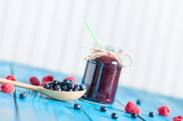 Blueberry jam in glass mason jar and fresh blueberries at wooden spoon. Light background, selective focus, Unique perspective — Stockfoto