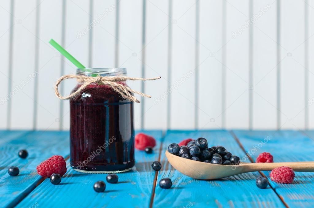 Mason jar with berry jam or marmalade and fresh raspberry on a rustic wooden table. Cooking background