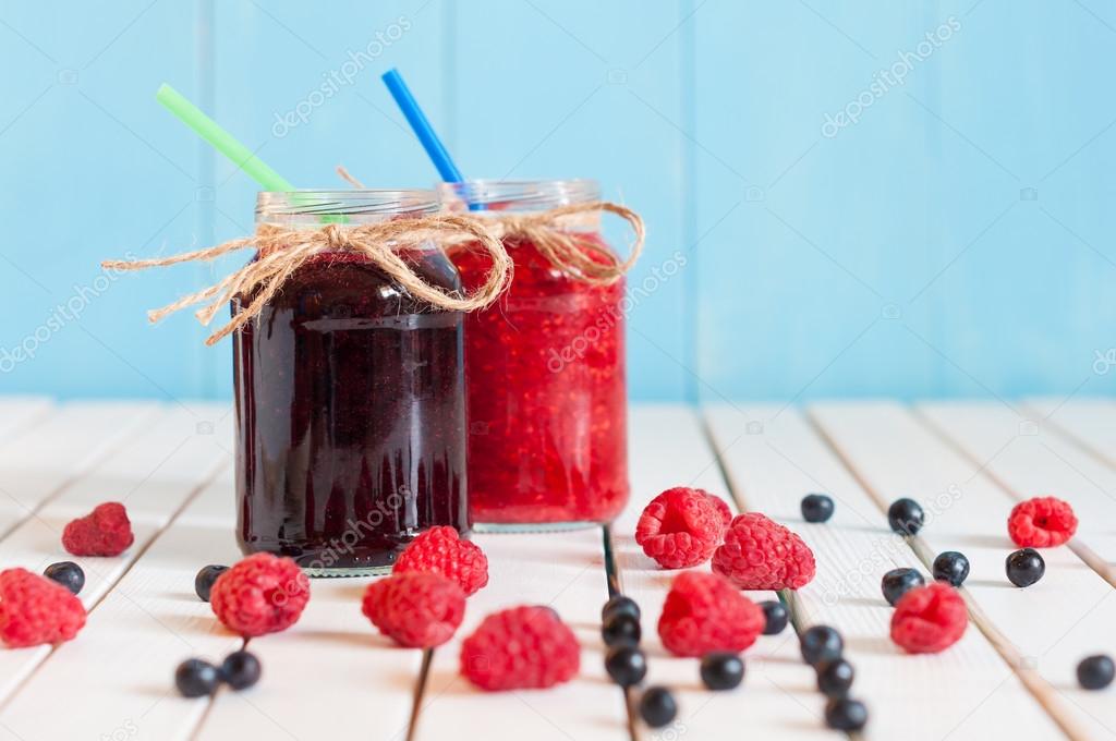 Rustic Mason Jars with raspberry jam and bog bilberry marmalade, fresh berries on white wooden background. 