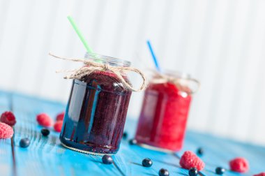 Glass mason jar with raspberry and blueberry jam. Fresh raspberries, blueberries on the blue wooden background.  Unique perspective, selective focus.