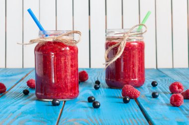 Glass mason jar with raspberry jam and fresh raspberries, blueberry on the blue wooden background