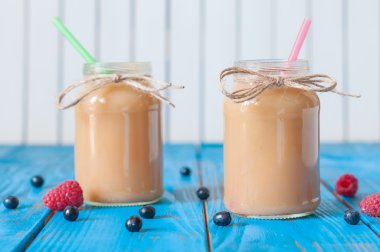 Peach and banana milkshake in mason jar with fresh raspberry, strawberry on the background of blue wooden boards. Selective focus