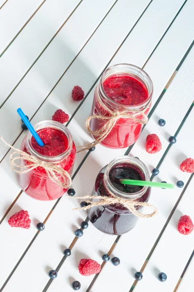 树莓、 草莓果酱、 蓝莓、 黑莓果酱在玻璃梅森罐子里，与新鲜浆果白色仿古木制的桌子上。顶视图，独特的视角 — 图库照片
