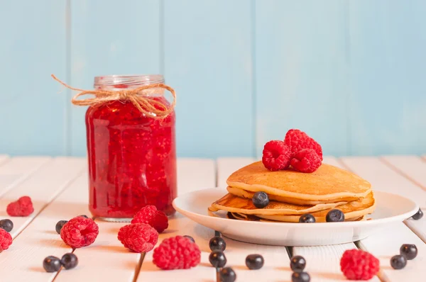 Stack of wheat golden pancakes or pancake cake with freshly picked blueberry on a dessert plate, glass mason jar full off raspberry jam. — Stock Photo, Image