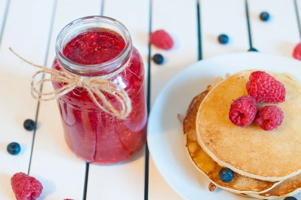 Empilement de crêpes dorées ou de galettes de blé avec framboises fraîchement cueillies dans une assiette à dessert et confiture de framboises dans un bocal à confiture. Vue du dessus — Photo