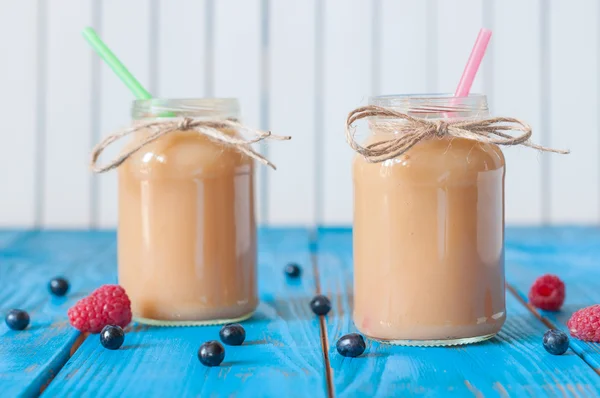 Peach and banana milkshake in mason jar with fresh raspberry, strawberry on the background of blue wooden boards. Selective focus — Stockfoto