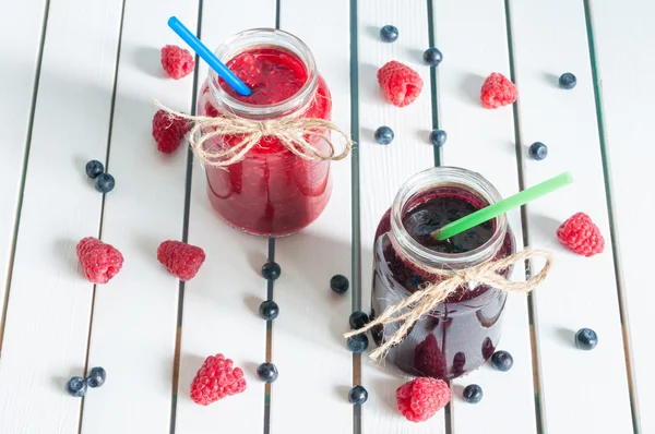 Framboise, confiture de fraises et de bleuets, confiture de mûres en pot de maçon en verre, avec des baies fraîches sur une table en bois rustique blanc. Vue de dessus, perspective unique — Photo