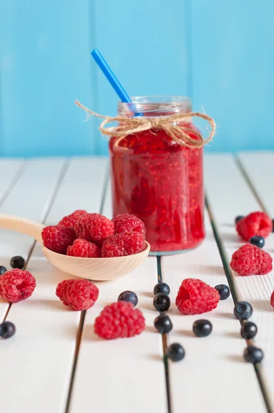 Raspberries in wood spoon. Crimson raspberry and jar of berry jam jn light wooden background. Selective focus — Stock Photo, Image