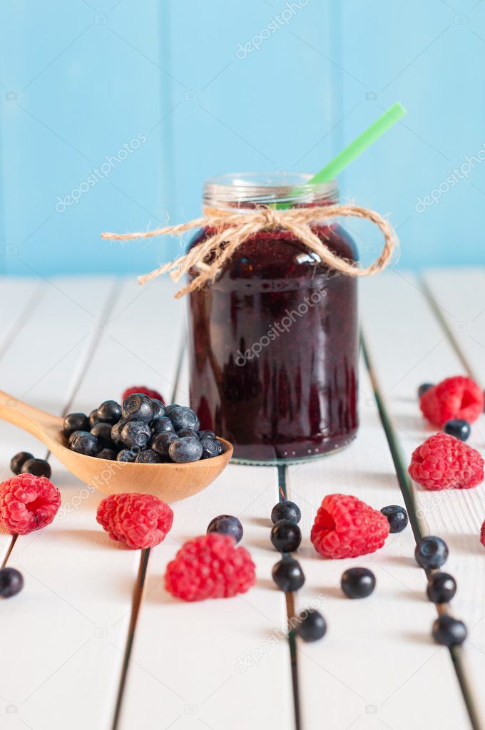 Bilberries in wood spoon. Crimson raspberry and jar of bilberry jam jn light wooden background. Selective focus