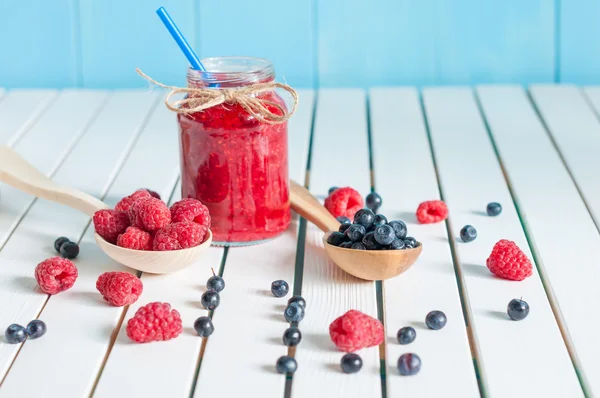 Raspberries in wood spoon. Crimson raspberry and jar of berry jam jn light wooden background. Selective focus — Stock Photo, Image