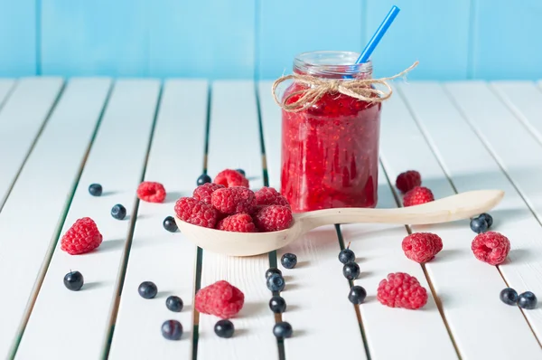 Tasty berries jam in mason jar on light wooden table with fresh raspberries and blueberries. Food background, selective focus — Stock Photo, Image