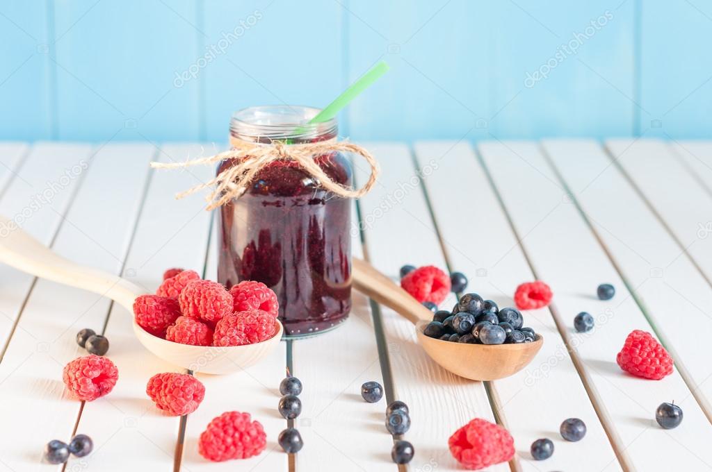 Blackberries jam in mason jar and fresh raspberry, blueberry on a wooden table. Macro image, selective focus