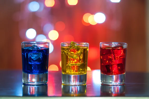 Three glasses with berry liqueur on the bar counter at a nightclub, magic light bokeh — Stock Photo, Image