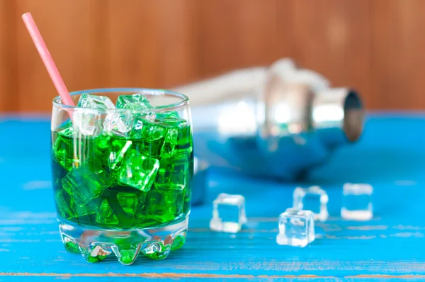녹색 알코올 칵테일 얼음 및 bluewooden 테이블에 셰이 커의 큐브를 닫습니다 — 스톡 사진