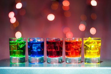 Five shots glasses full of assorted beverages and ice on golden blurred lighting bokeh background clipart