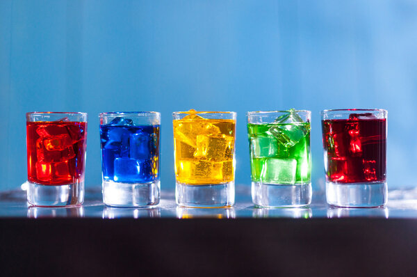 Bright alcohol drinks or berries cocktail in different colours, glasses tumbler on wooden backfround