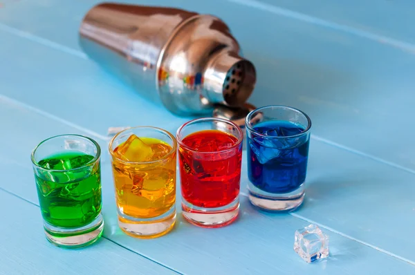 Blue, yellow, green, red alcohol or alcohol-free cocktail with ice cubes and shaker on a bar counter, wooden background. — Stock Photo, Image