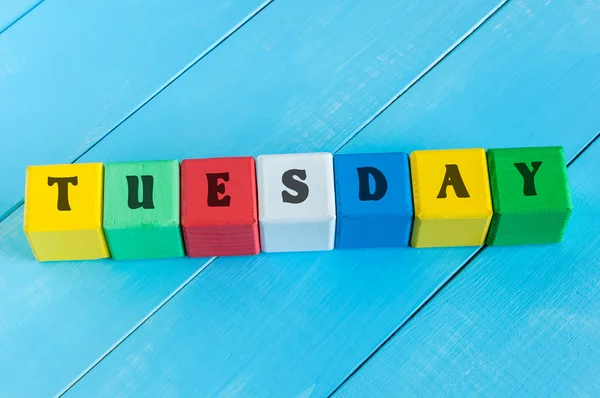 The word TUESDAY written in wooden color cubes on light blue wood background — Stock Photo, Image