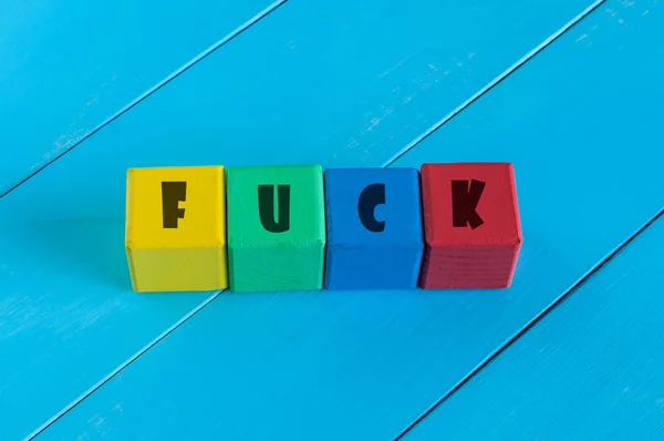Fuck - word on childrens colourful cubes or blocks. Colourful wooden background — Stockfoto
