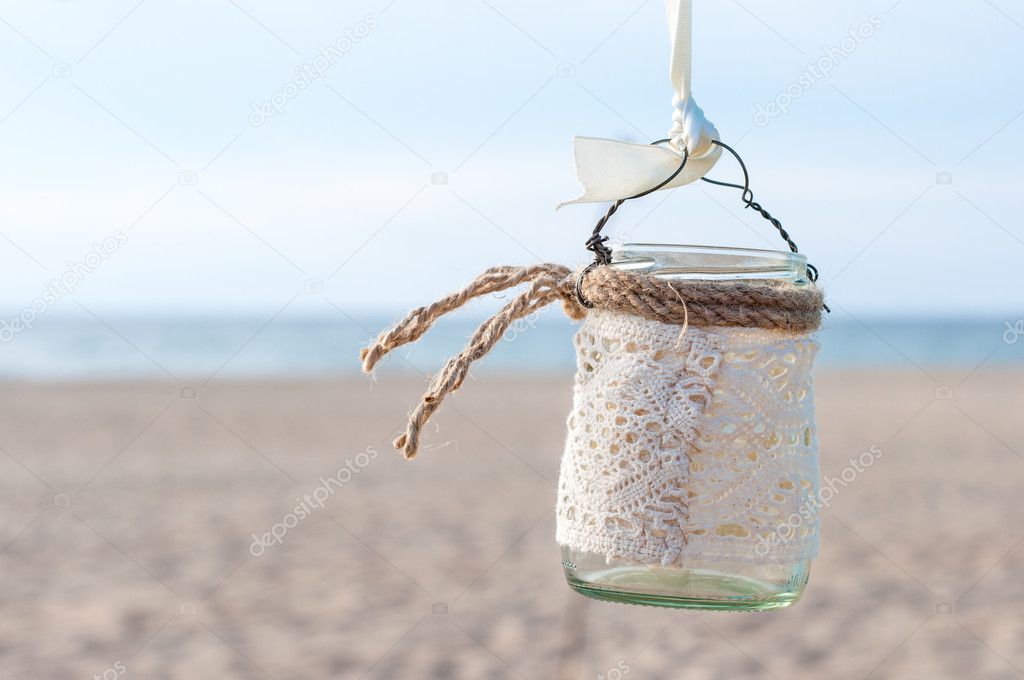 Glass lantern decorated with white lace hanging on wedding archway. Sea background