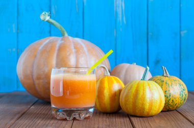 Pumpkin juice in a glass with many different pumpkins on  wooden boards background