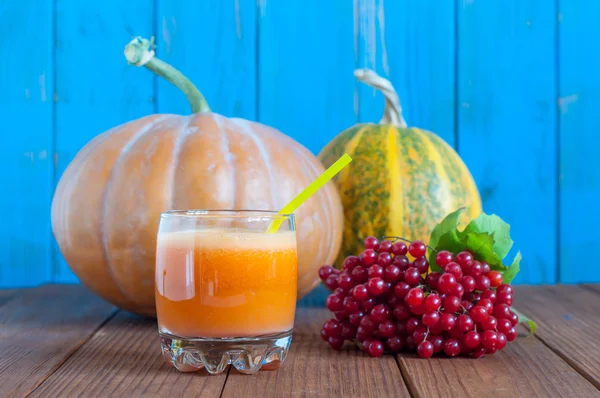 Fresh pumpkin juice with two whole pumpkins and rowan berry branch on bright blue wooden background. Autumn harvest view — Stok fotoğraf