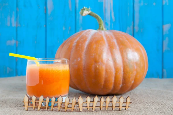 Bebida de calabazas con gran calabaza naranja detrás de una valla rústica en miniatura sobre fondo de madera rural. Otoño comida saludable —  Fotos de Stock
