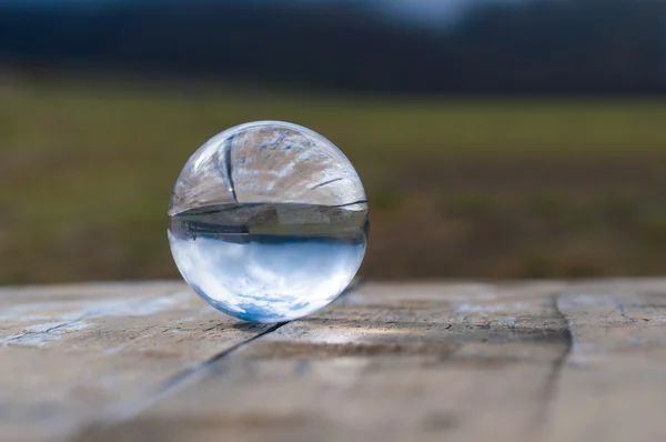 Glass transparent ball on dark green background and wooden surface. Soft focus. With empty space for text — Stock Photo, Image