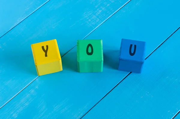 YOU - sign on color wooden cubes with light blue wood background. — Stock Photo, Image