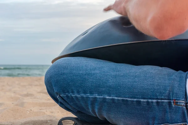 Relax music background. Hands percussion. Musician sit on sand and play the Hang or handpan with sea On Background. The hang is a traditional ethnic drum musical instrument — Stock fotografie