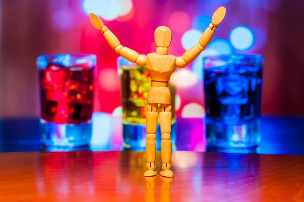 Happy wooden dummy, mannequin or man figurine, silhouette stand against the backdrop of alcohol drinks. Friday background — Stock fotografie