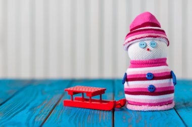Red sled and little handmade snowman on light wooden background. New Year card with empty space for text