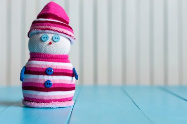 Funny little handmade snowman in a white and marsala stripy sweater on wooden background. Christmas time, New year postcard with empty space