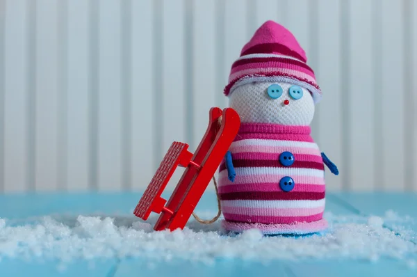 Сніговик ручної роботи в марсаловому кольоровому светрі з червоними санчатами на снігу Взимку. Різдвяний фон листівки, порожнє місце для тексту — стокове фото