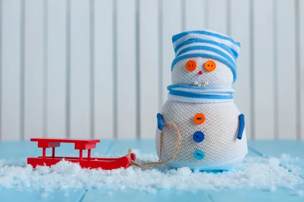 Handmade snowman in striped cap with red sled on snow In winter. Christmas postcard background, empty space for text — Stockfoto