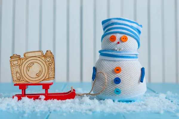 Сніговик ручної роботи в смугастій шапці з червоними санчатами та іграшковою камерою на снігу Взимку. Різдвяний фон листівки, порожнє місце для тексту — стокове фото
