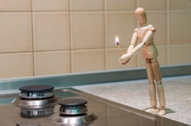 Wooden dummy, mannequin or man figurine holding a burning match and tryi to light Or ignite gas stove. No Gas because of debt for utilities
