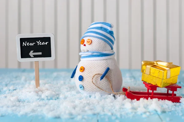 New Year is coming concept.  Snowman with red sled and gift or present stand near written on direction sign new year