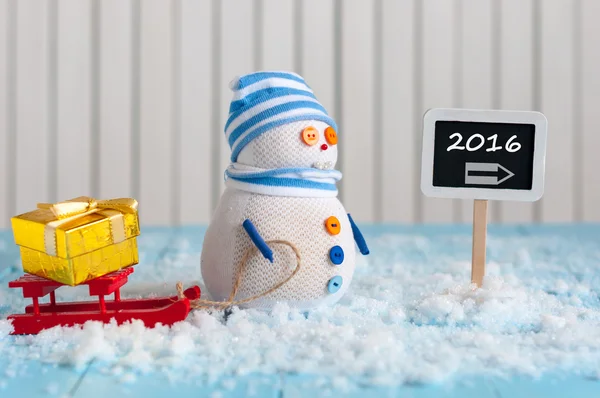 New Year 2016 is coming concept.  Snowman with red sled stand near written on direction sign 2016. — стокове фото