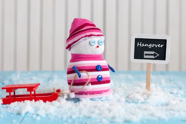 New Years hangover concept. Snowman with red sled stand near direction sign Hangover. Postcard — Stok fotoğraf