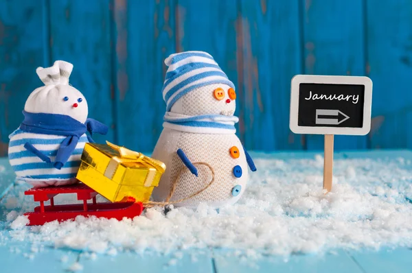 Word januari geschreven richting teken en sneeuwpop met rode slee. Kerstmis, Nieuwjaar, winter decoraties. — Stockfoto