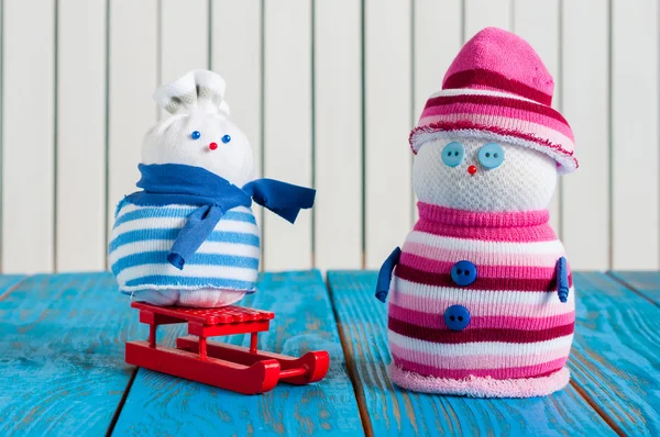 Rode slee en twee kleine handgemaakte sneeuwpop op lichte houten achtergrond. Xmas card met lege ruimte voor tekst — Stockfoto