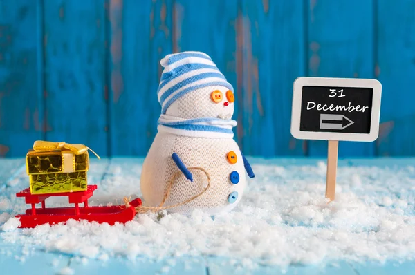 Nieuwjaar is komende concept. Sneeuwpop met rode slee en xmas giftnear bord 31 December. Kerstmis, Nieuwjaar decoraties. — Stockfoto