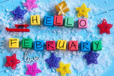 writing hello february on toy wooden colour cubes with decor and light blue background