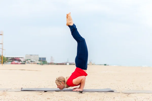 Sporty beautiful blond woman in sportswear working out indoors, doing yoga chin balance Ganda Bherundasana or Scorpion on coast background — Stock fotografie